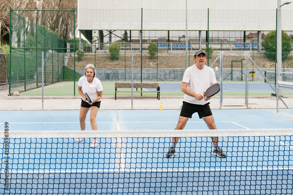 Obraz premium Senior couple enjoying an energetic game of pickleball, staying active and healthy on an outdoor sports court