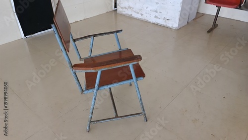 Worn classroom chair with missing wooden armrest and rusted metal frame