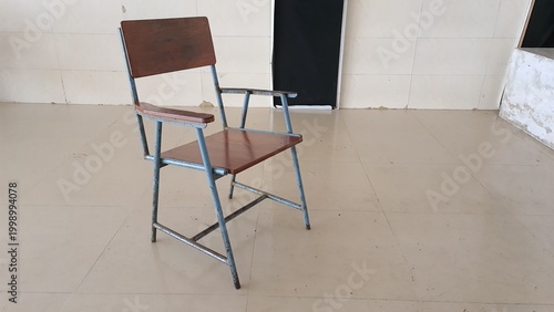 Worn classroom chair with missing wooden armrest and rusted metal frame
