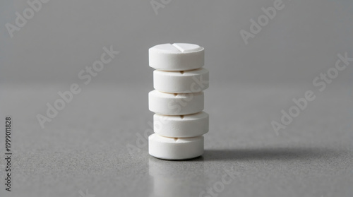 White tablet stack on gray surface, medicine pill concept with minimal studio light
