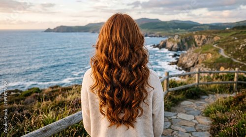 Coastal cliff view back view woman long wavy hair seaside landscape ocean horizon rocky shore scenic coastline standing alone sweater travel