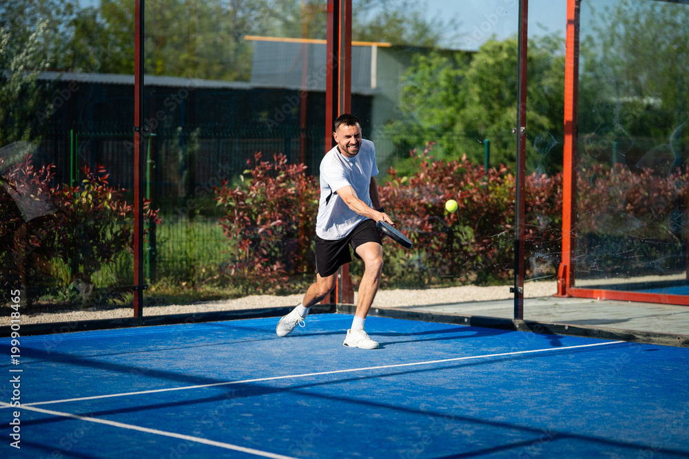 Fototapeta premium Man playing padel on blue court, hitting ball