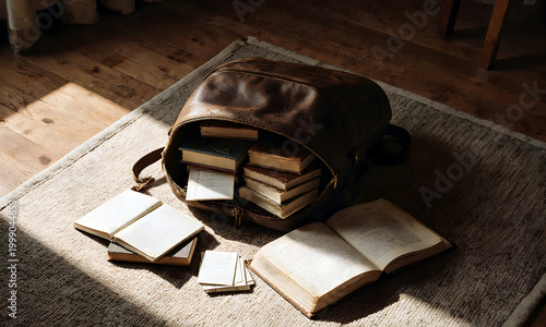Open leather backpack with books on a rug in cozy indoor setting  