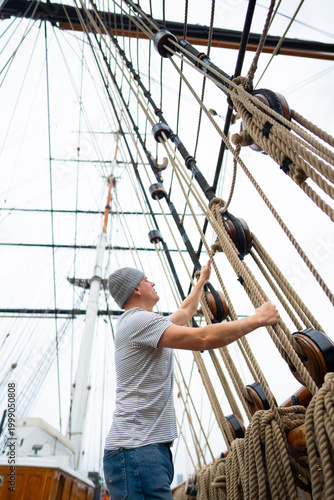 фотографія A man works on tying ropes on a tall ship in a harbor