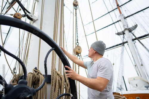 Fotografie A man stands on a tall ship and adjusts the ropes and lines