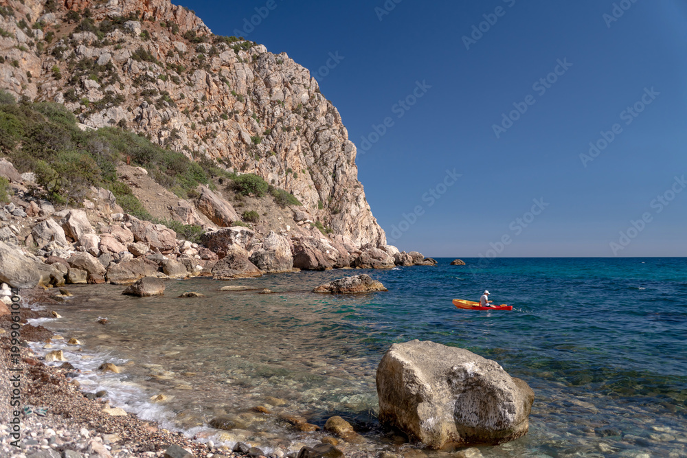 Fototapeta premium Kayak coastline sea person paddling orange kayak along a beautiful rocky coastline peaceful summer adventure clear turquoise water