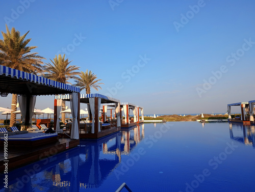 Striped cabana sunbeds in the shaded area by the swimming pool by the sea on Saadiyat island in Abu Dhabi