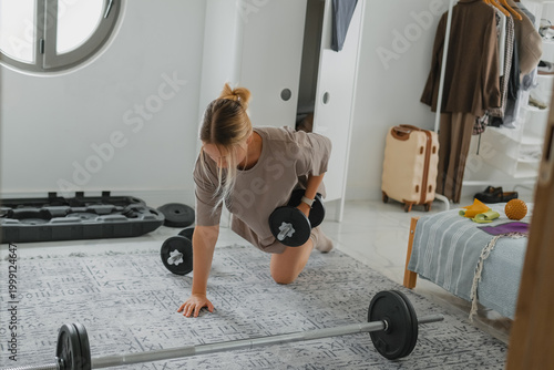 Fotografia Woman doing strength workout with dumbbells at home, home gym, fitness routine, active lifestyle, women fitness and functional training concept