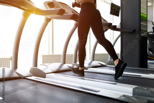 Obraz na plátně Closeup of young Black womans legs running on treadmill in gym, wearing black le