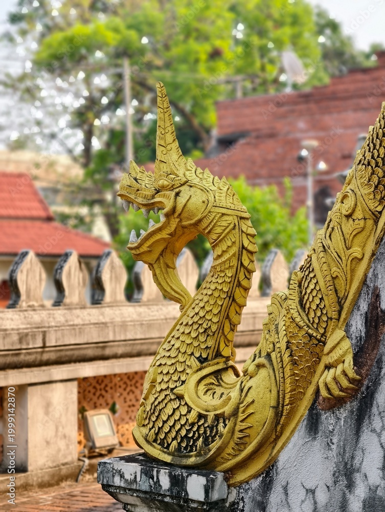 Fototapeta premium Golden Serpent: A meticulously crafted golden serpent sculpture adorns an ornate temple roof, reflecting the intricate details and vibrant artistry of the sacred architecture.