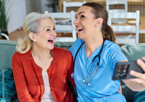 Doctor or nurse caregiver helping senior woman with a mobile phone taking selfie at home or nursing home