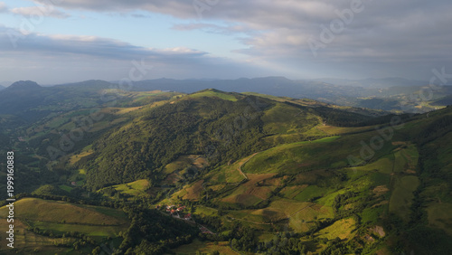Cantabrian green hills and valleys bathed in warm morning light under a dramatic cloudy sky, serene rural landscape from above
