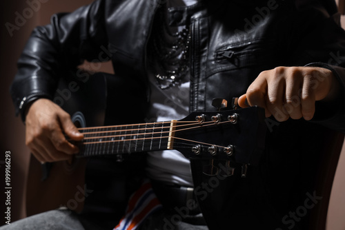 Foto Young man in leather jacket playing guitar on brown background