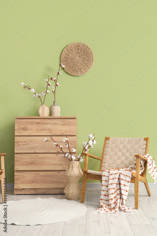 Obraz premium Wicker armchair, chest of drawers and vases with cotton flowers in interior of living room