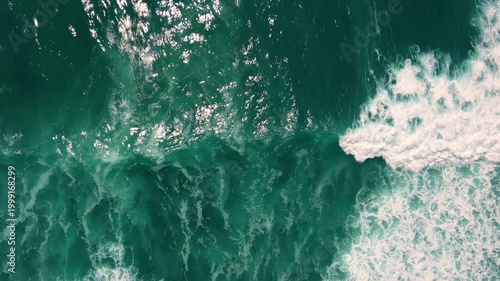 Aerial shot of the ocean with waves doing swirls and patters, rocks, sand and beach