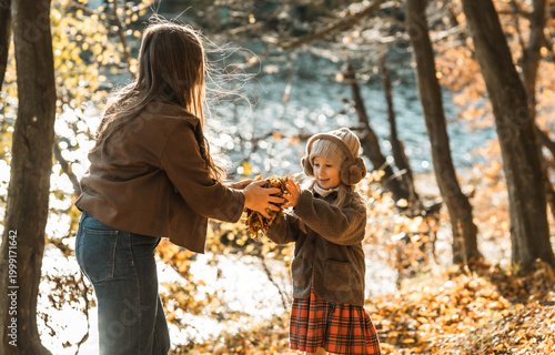 Authentic moment of joy: woman and child throwing yellow leaves in autumn nature, family bonding and happiness.
