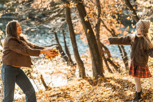 Authentic moment of joy: woman and child throwing yellow leaves in autumn nature, family bonding and happiness.
