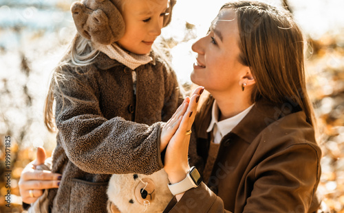 Happy mother and daughter holding hands and smiling at each other in beautiful autumn forest.