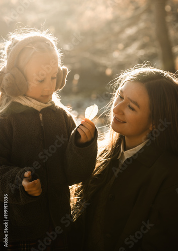 Curious little girl showing a bright yellow autumn leaf to her mother while walking in the forest.
