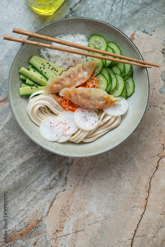 Dumpling, vegetable and noodle bowl on a grey and roseate granite background, vertical shot with space, flat lay