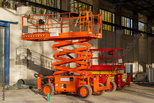 Two orange scissor lifts of different sizes parked inside an old industrial warehouse hall