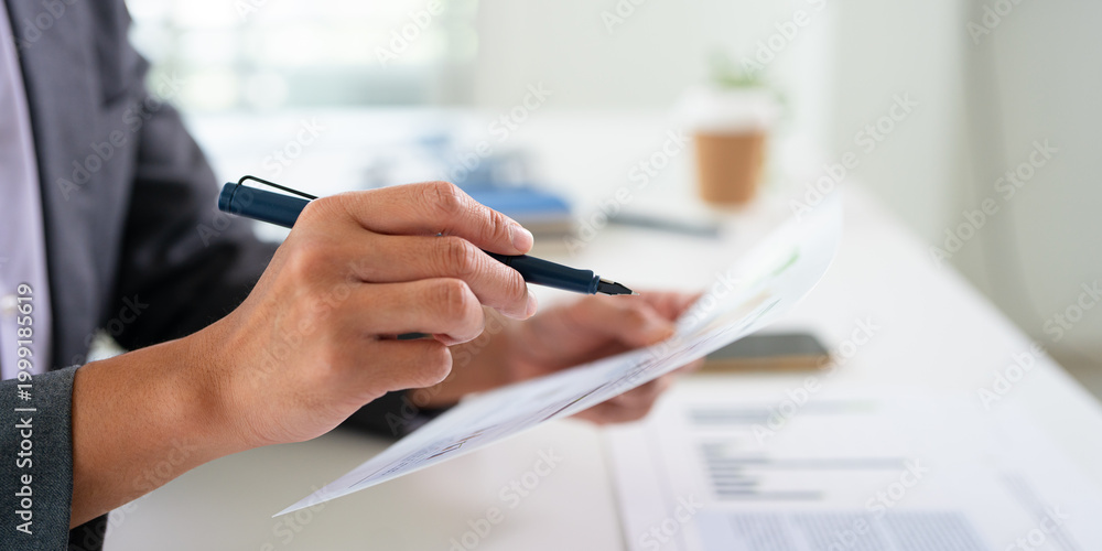 Fototapeta premium Close up hnads holding pen reviewing document papers at desk.