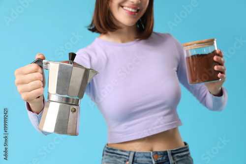 Beautiful young woman with geyser coffee maker and jar of ground coffee on bl...