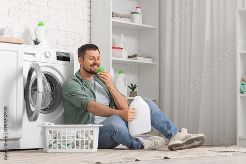 Fotografía Young man smelling laundry detergent near washing machine at home