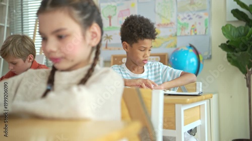 Students turn to retrieve their stationery from backpacks hanging behind their chairs, while students and teachers of diverse nationalities are engaged in activities in the background of this internat