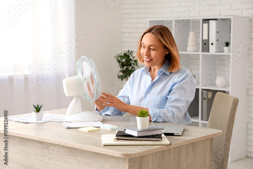 Fotografía Beautiful mature happy businesswoman with electric fan in office