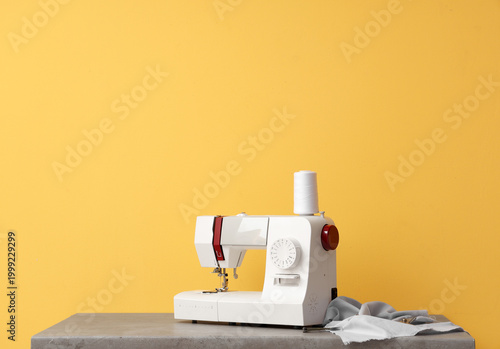 Obraz na plátne Modern sewing machine with fabric on yellow background