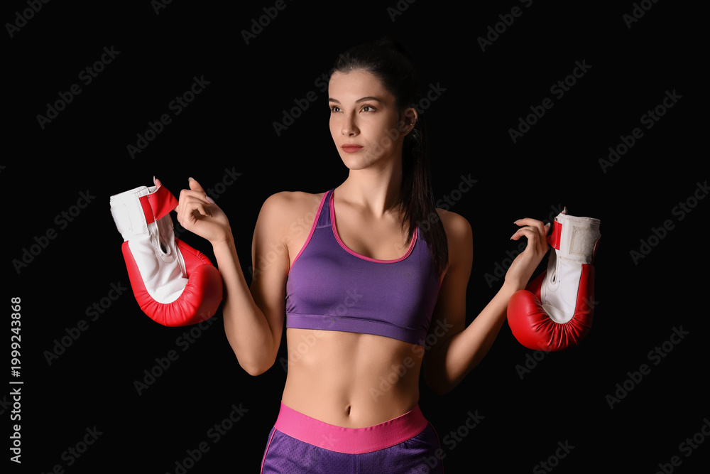 Fototapeta premium Confident young woman with boxing gloves on black background