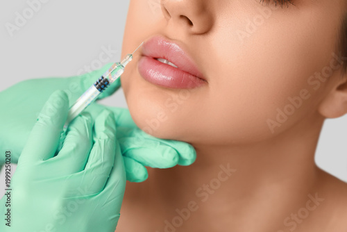 Fényképezés Young woman receiving lip injection on grey background, closeup