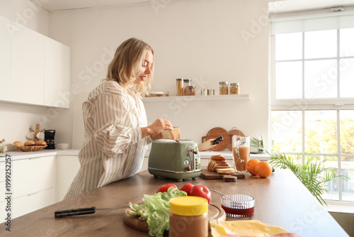 Young beautiful happy woman making tasty toasts in kitchen