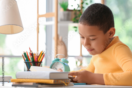 Little African-American boy reading schoolbook at home