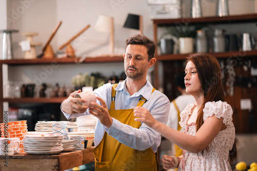 Bild auf Leinwand Pottery shop assistant and customer choosing ceramic cup in craft store interior