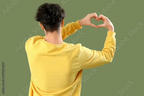 Handsome young man making heart with his hands on green background, back view