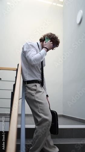 Vertical screen office worker walks down stairs talking on phone with family after long work day feeling tired but connected balancing career pressure and personal life through distant communication