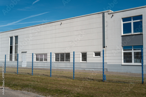 White industrial building with security fence under blue sky