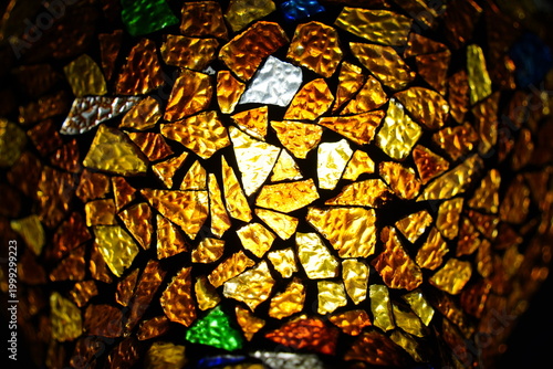 Close-up of colorful mosaic glass texture with warm light, glowing amber and gold stained glass fragments for decorative artistic background.