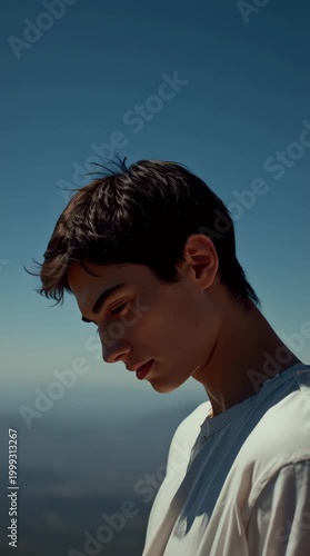 Young man looking down with a pensive expression against a clear blue sky