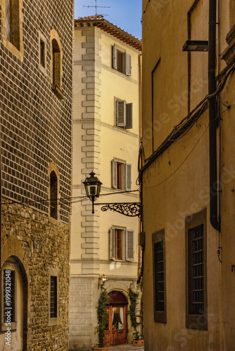 Historic Narrow Florentine Street Alley In Italy With Ancient Stone And Sgraffito Building Facades A Lamp Post And Traditional Wooden Shutters Under A Warm Evening Sky