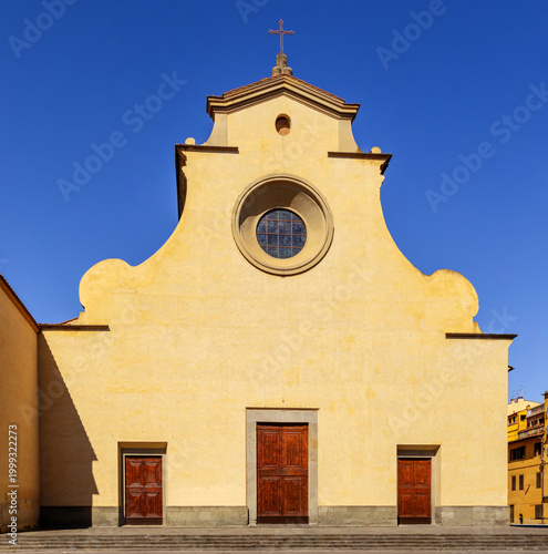 Facade Of The Church Of Santo Spirito In Florence With Distinctive Semicircular Top Rose Window Three Doors And Simple Ochre-Yellow Stucco Under A Deep Blue Sky