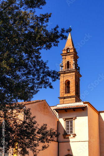 Historical Brick Bell Tower Of Santo Spirito Church In Florence Italy Against A Deep Blue Sky On A Sunny Day With An Old Building And A Tree In The Foreground