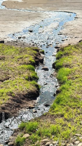 Small polluted stream flowing into shallow river, low water level and drought conditions with environmental impact in landscape