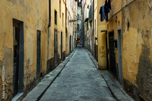 Narrow Medieval Street In Florence Italy With Yellow Weathered Buildings And Cobblestones
