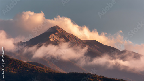 Majestic mountain peak illuminated by golden hour sunlight amidst dramatic clouds and blue sky during sunrise or sunset.