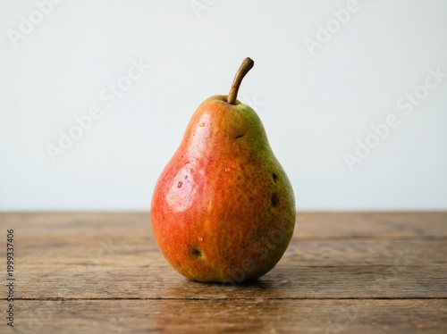 A ripe red and yellow pear with water drops on a rustic wooden table against a white background
