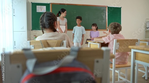 Schoolgirl presenting in front of class with teacher observing and classmates listening, representing communication skills and confidence in learning