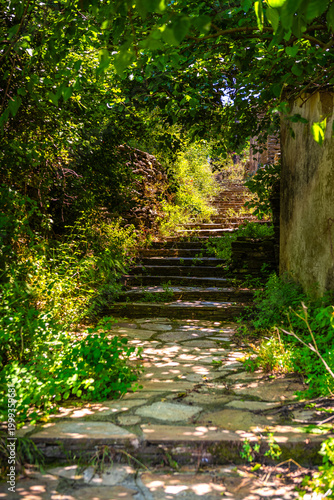 Empty stone passage alley staircase in Perdiki village, Ikaria, Greece Greek island on sunny summer day by old stone buildings